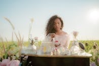 Woman Sitting at Table in Middle of Meadow and Producing Perfumes from Flowers