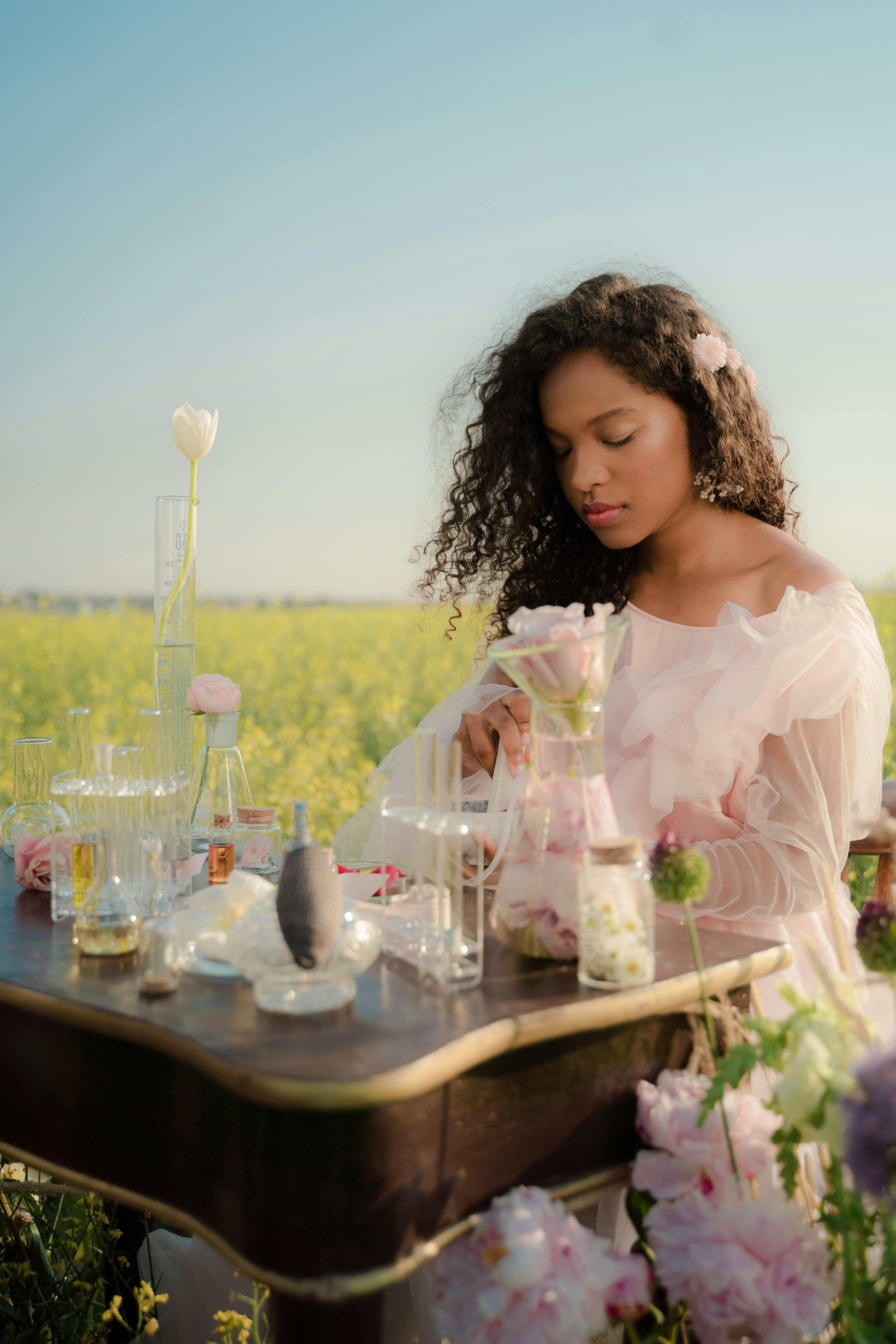 young woman in airy summer dress creating perfumes in flower field laboratory