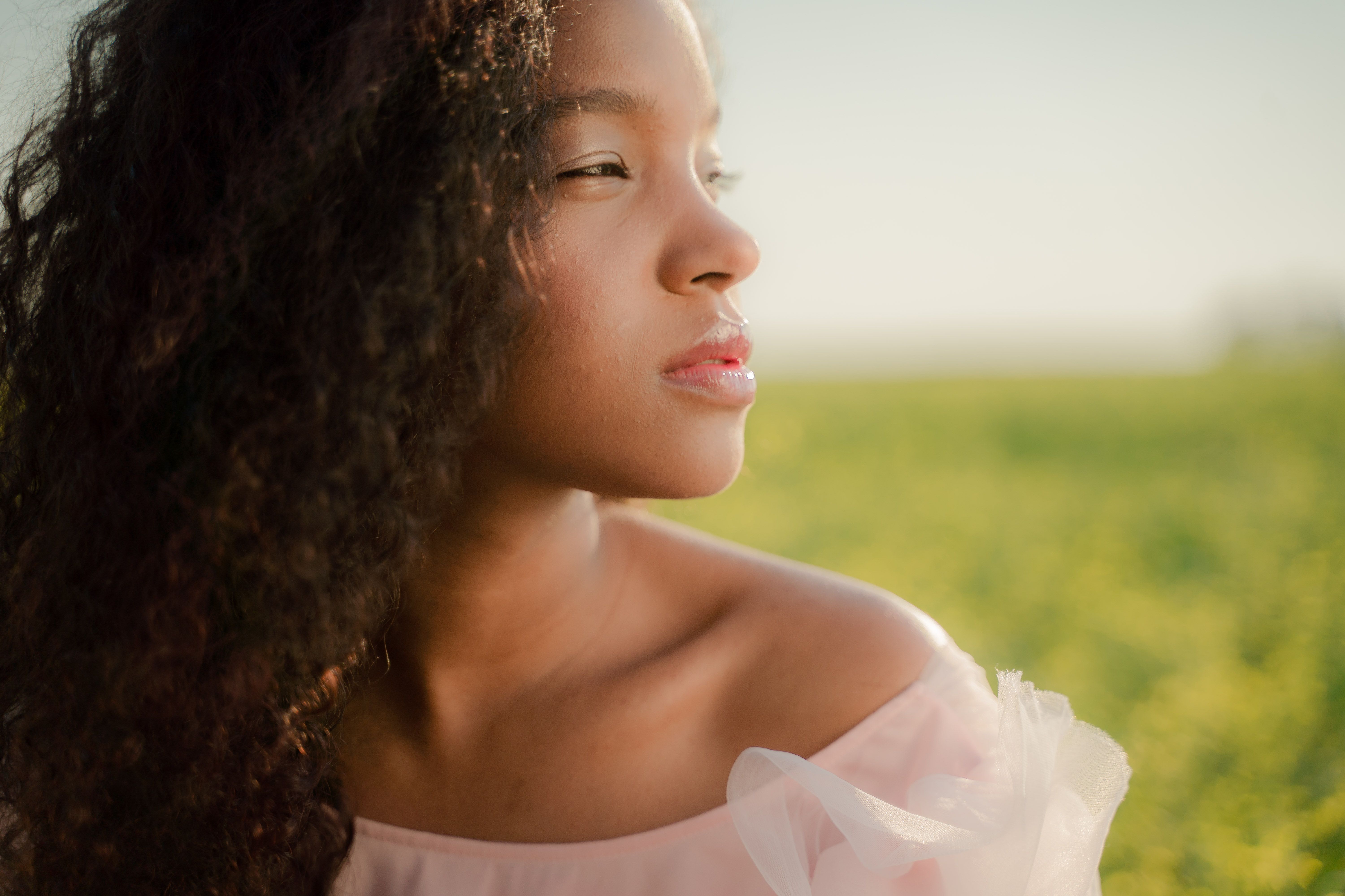 Serene female portrait with curly hair in a sunny meadow.