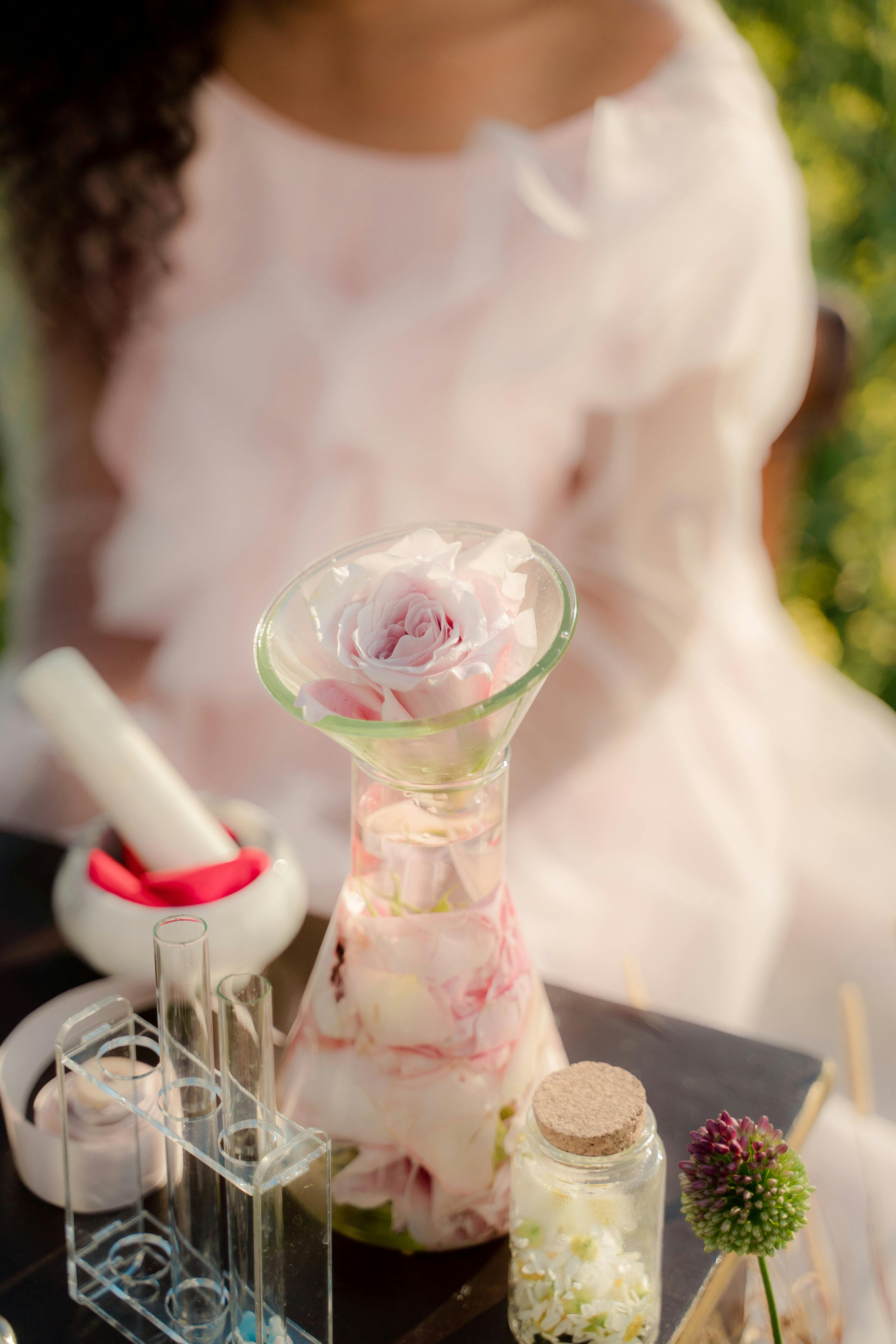 unrecognizable woman sitting at table with glass flask full of rose petals