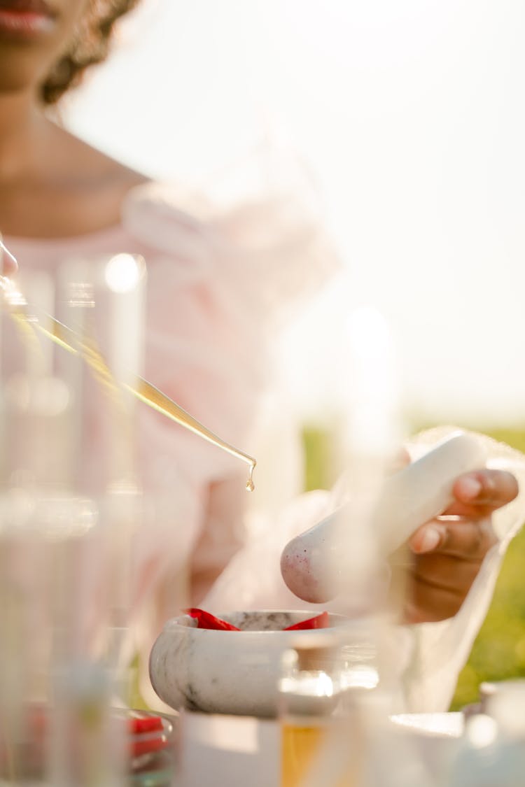 Unrecognizable Woman Adding Oil With Pipette To Mortar With Red Substance