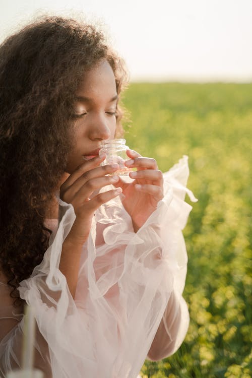 Woman on a Meadow Smelling a Liquid in a Glass