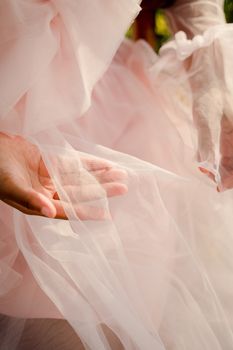 Close-up of a woman's hand gently holding soft pink tulle fabric, showcasing delicate details and texture.