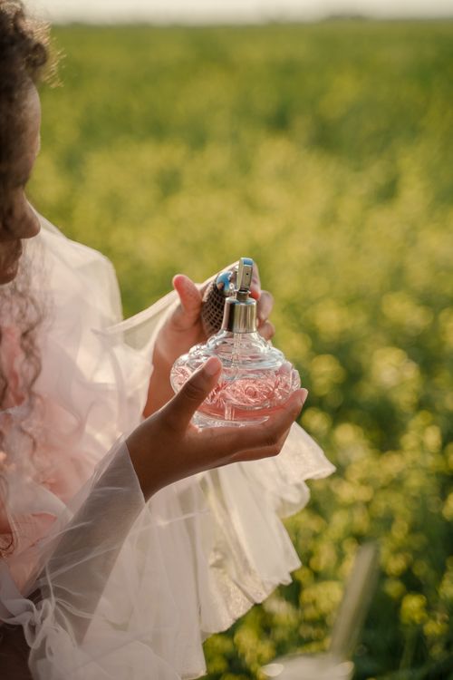 Free A woman in a dress holds a perfume bottle in a sunny, blooming field. Stock Photo