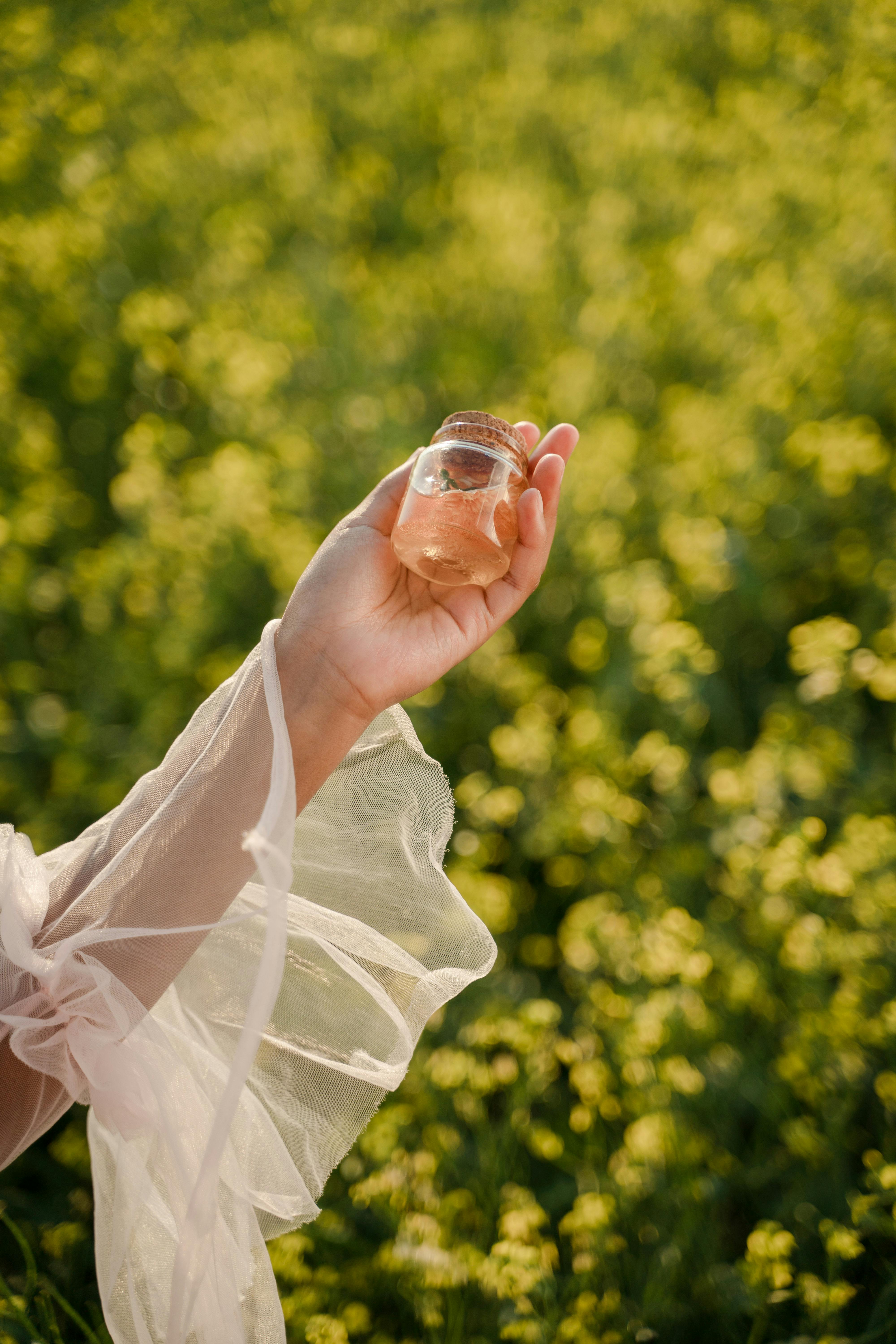 A delicate hand holds a perfume bottle against a vibrant green and yellow floral background.