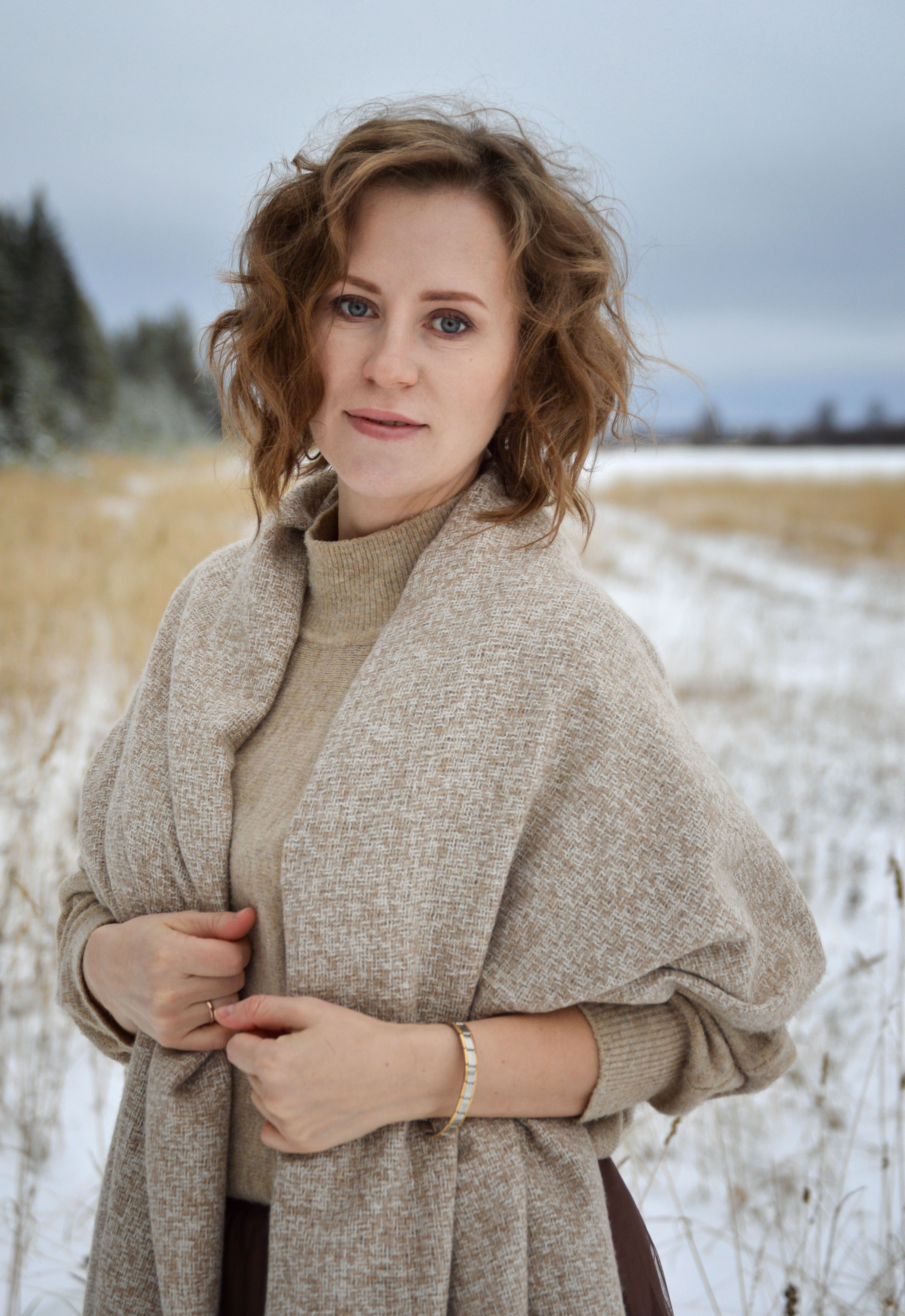A woman poses warmly in a snow-covered field wearing a stylish coat, exuding elegance.