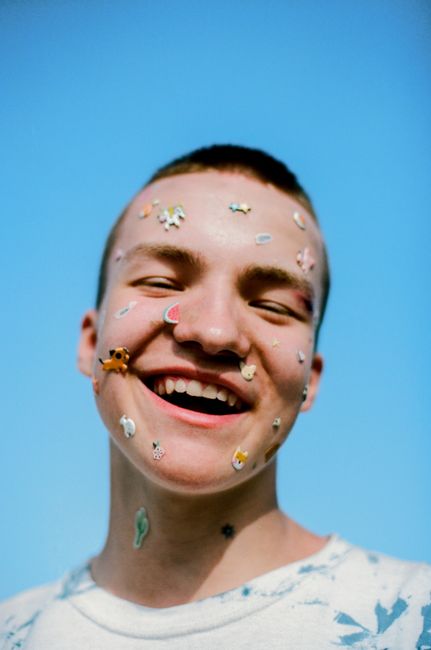 Happy teenager with face stickers smiling outdoors against a clear blue sky. Vibrant and playful portrait.