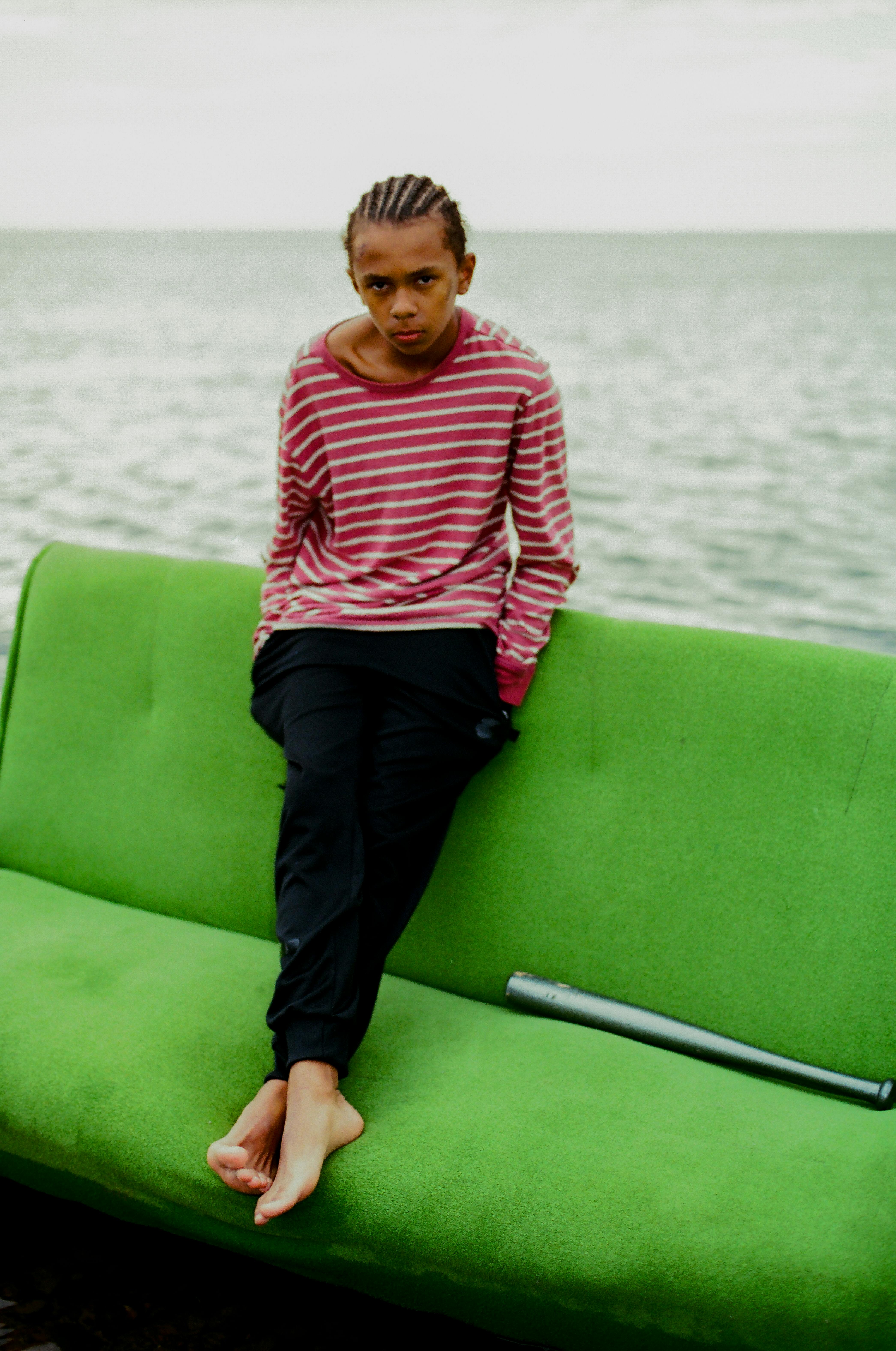 photo of a boy in a striped shirt sitting on a green couch