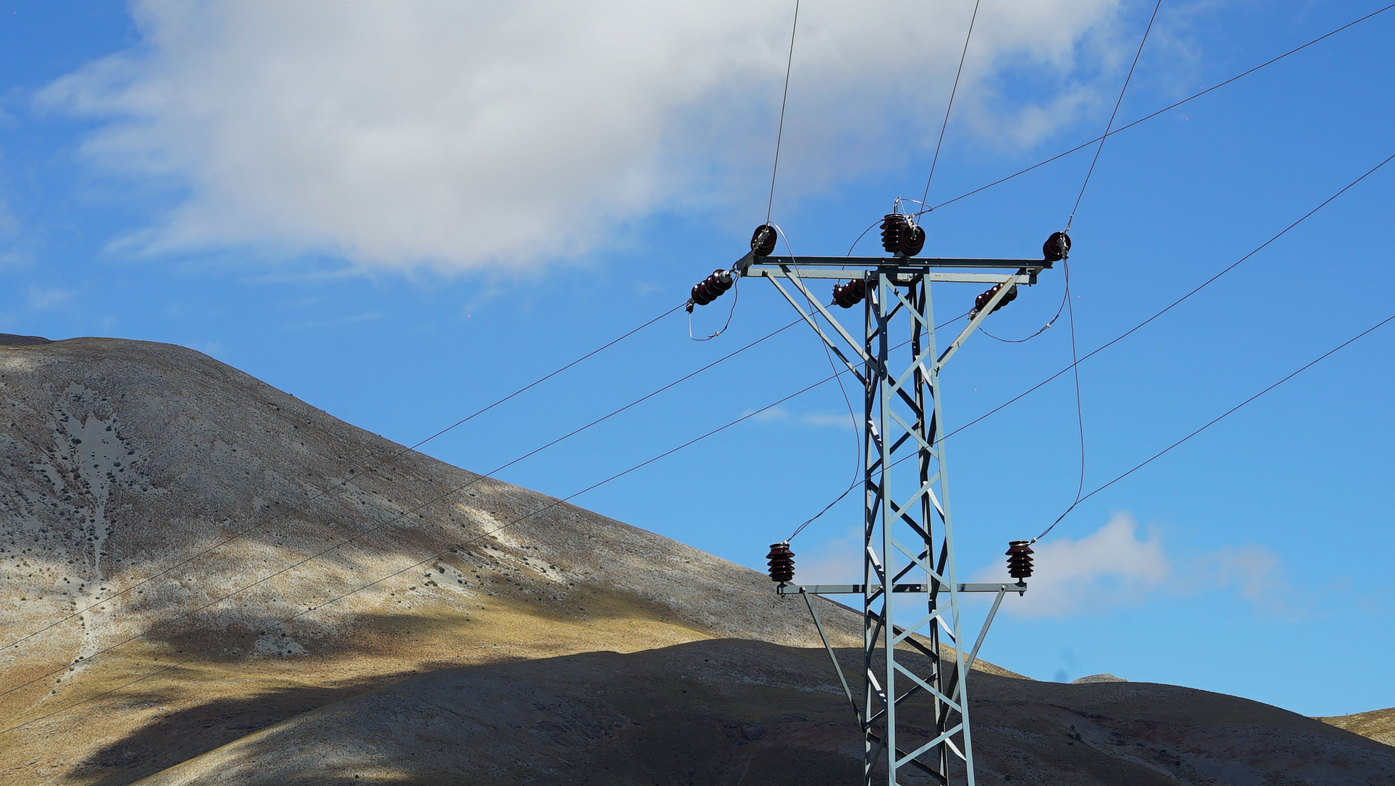 Majestic mountain landscape with a tall power line tower under a clear blue sky.