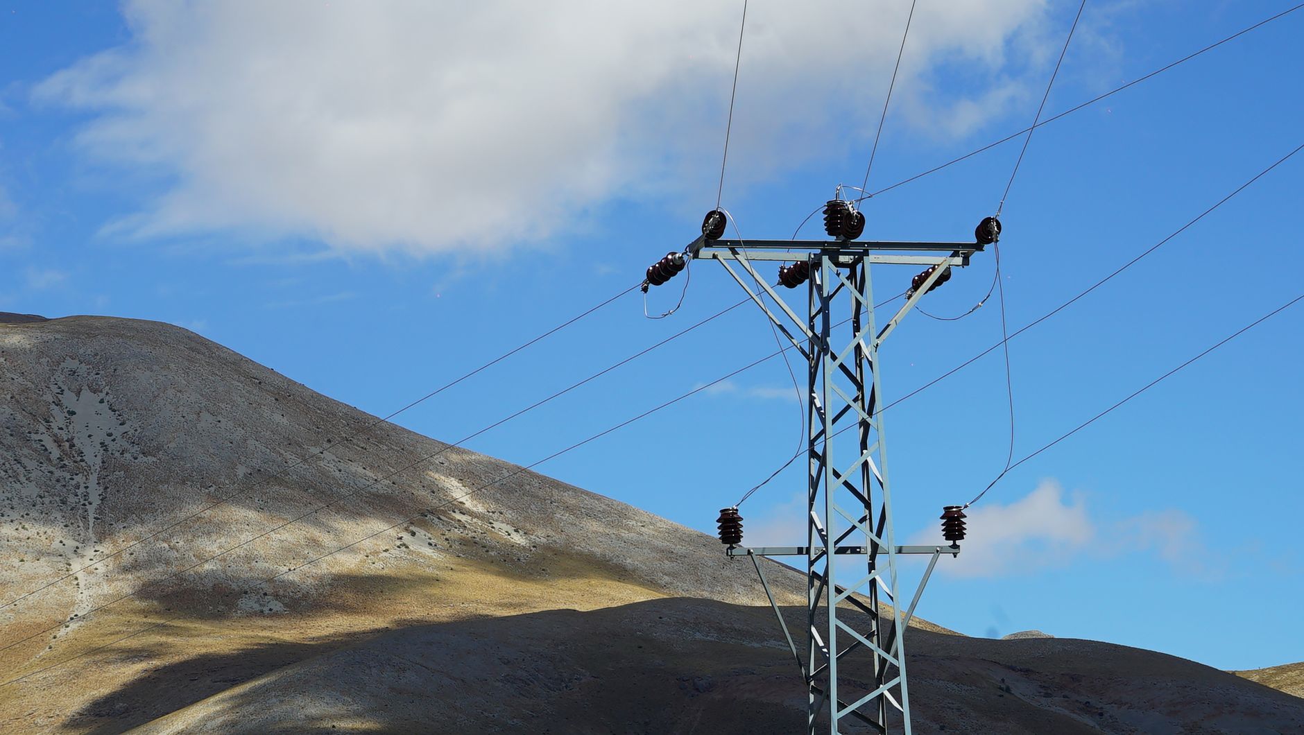 Majestic mountain landscape with a tall power line tower under a clear blue sky.