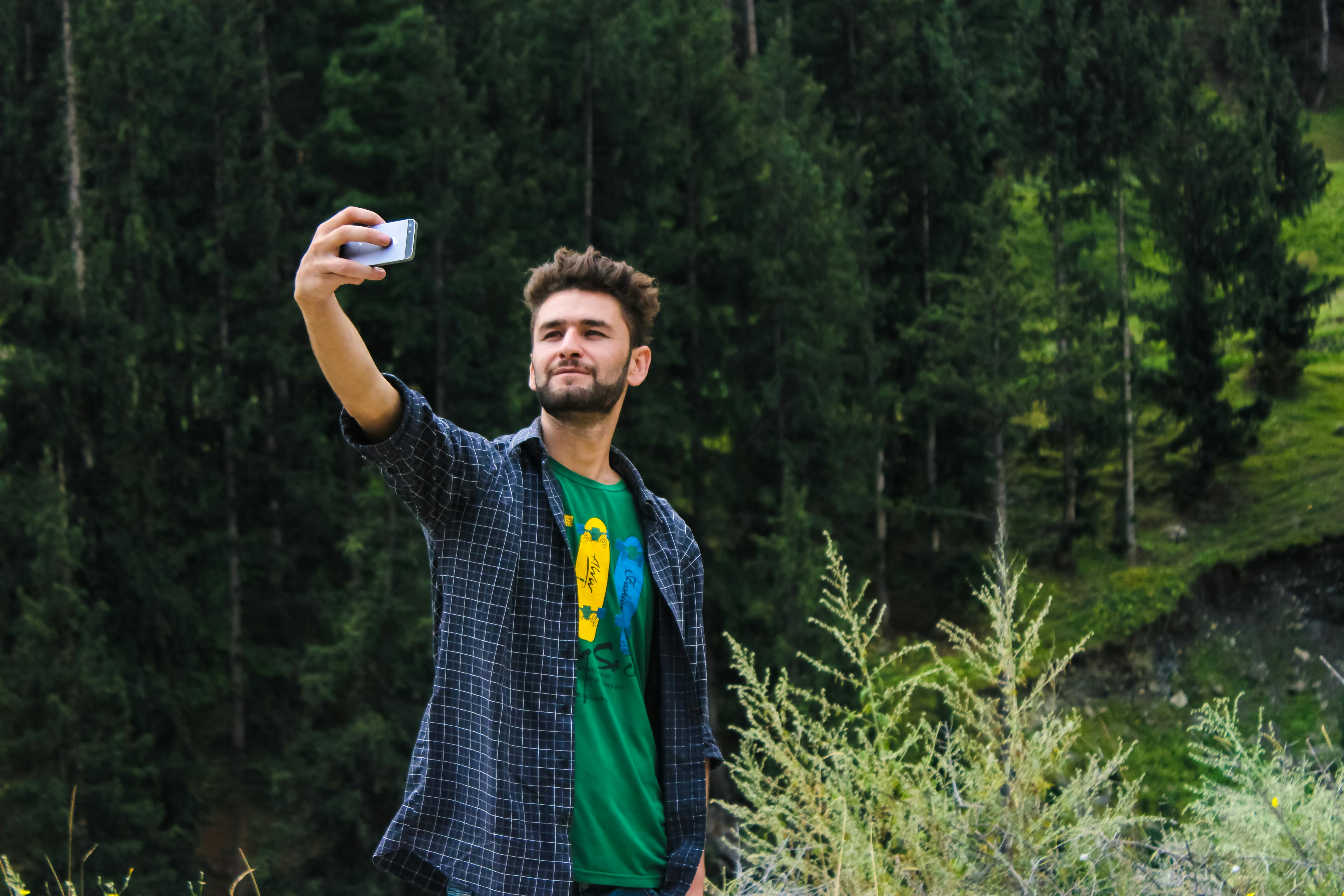 Man in Blue Sports Shirt and Green Top Taking a Selfie Near Green Trees
