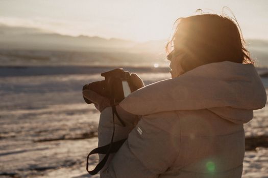 Woman capturing the serene sunset on a snowy beach at Курай, Altai Republic, Russia.