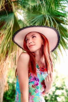 Elegant woman in a floral dress posing outdoors under palm leaves in Athens, Greece.
