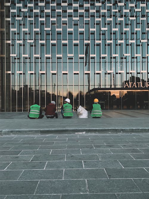 Workers Sitting on the Concrete Pavement Near the Glass Facade Building
