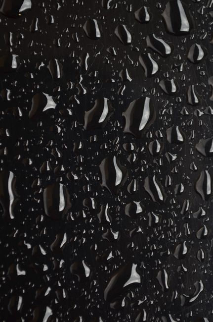 Macro shot of water droplets on a black surface, showcasing texture and detail.