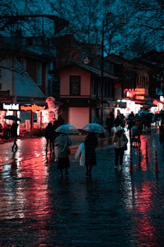 Evening street scene in Bursa, Turkey with people and umbrellas reflecting on wet pavement.