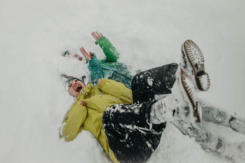 High-Angle Shot of Two People in Winter Clothes Lying on Snow-Covered Ground