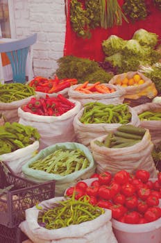 Colorful sacks of fresh produce at an outdoor market, showcasing vibrant tomatoes, peppers, and greens.