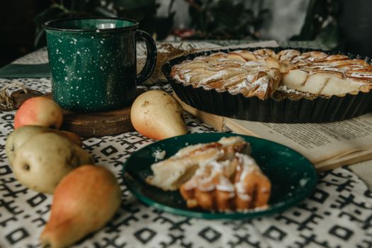 A delicious apple and pear tart with a green mug on a patterned tablecloth.