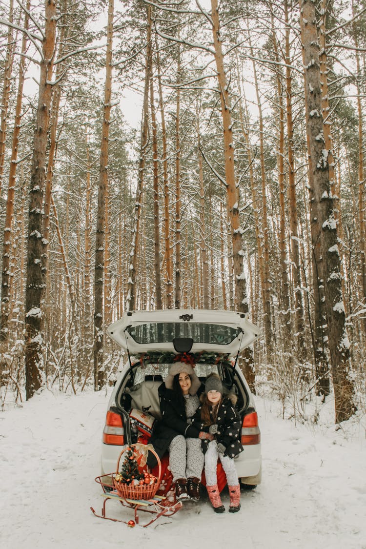 Mother And Daughter In Winter Clothes Sitting In Car Trunk