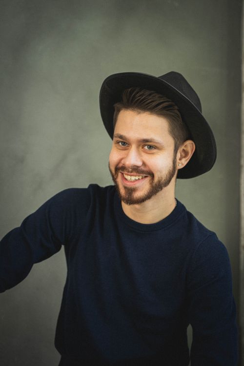 Free Portrait of a smiling man wearing a black hat and dark sweater against a studio background. Stock Photo