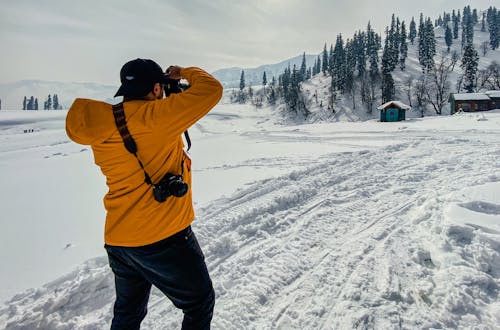 Man in Yellow Jacket Taking Photos on Snow Covered Field