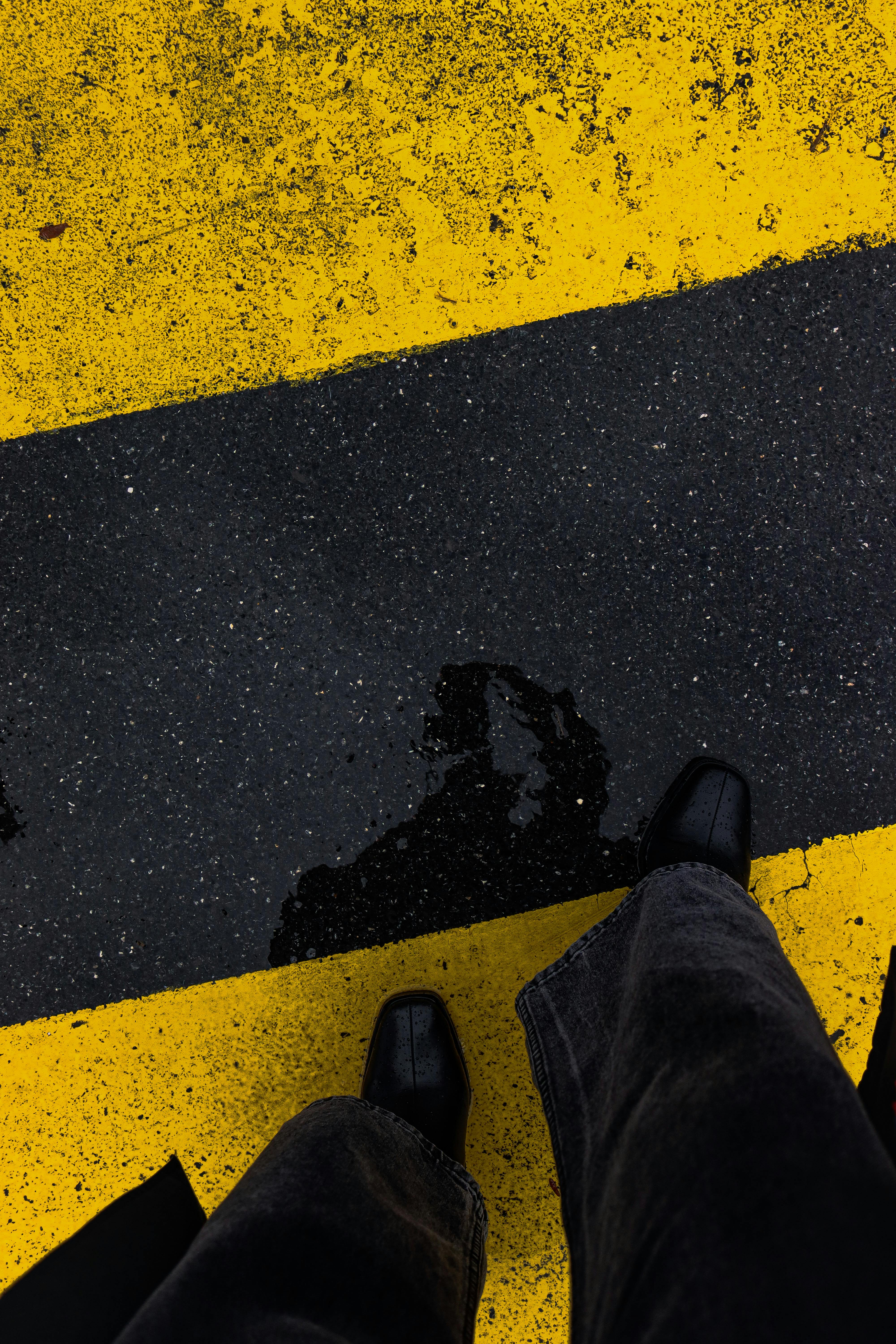 High angle view of a person's reflection in a puddle on a yellow-painted pedestrian lane in Lyon, France.