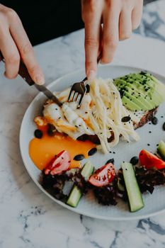 Top view of a gourmet brunch plate featuring avocado toast, poached egg, cheese, and fresh salad.