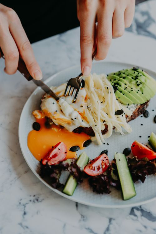 Free Top view of a gourmet brunch plate featuring avocado toast, poached egg, cheese, and fresh salad. Stock Photo