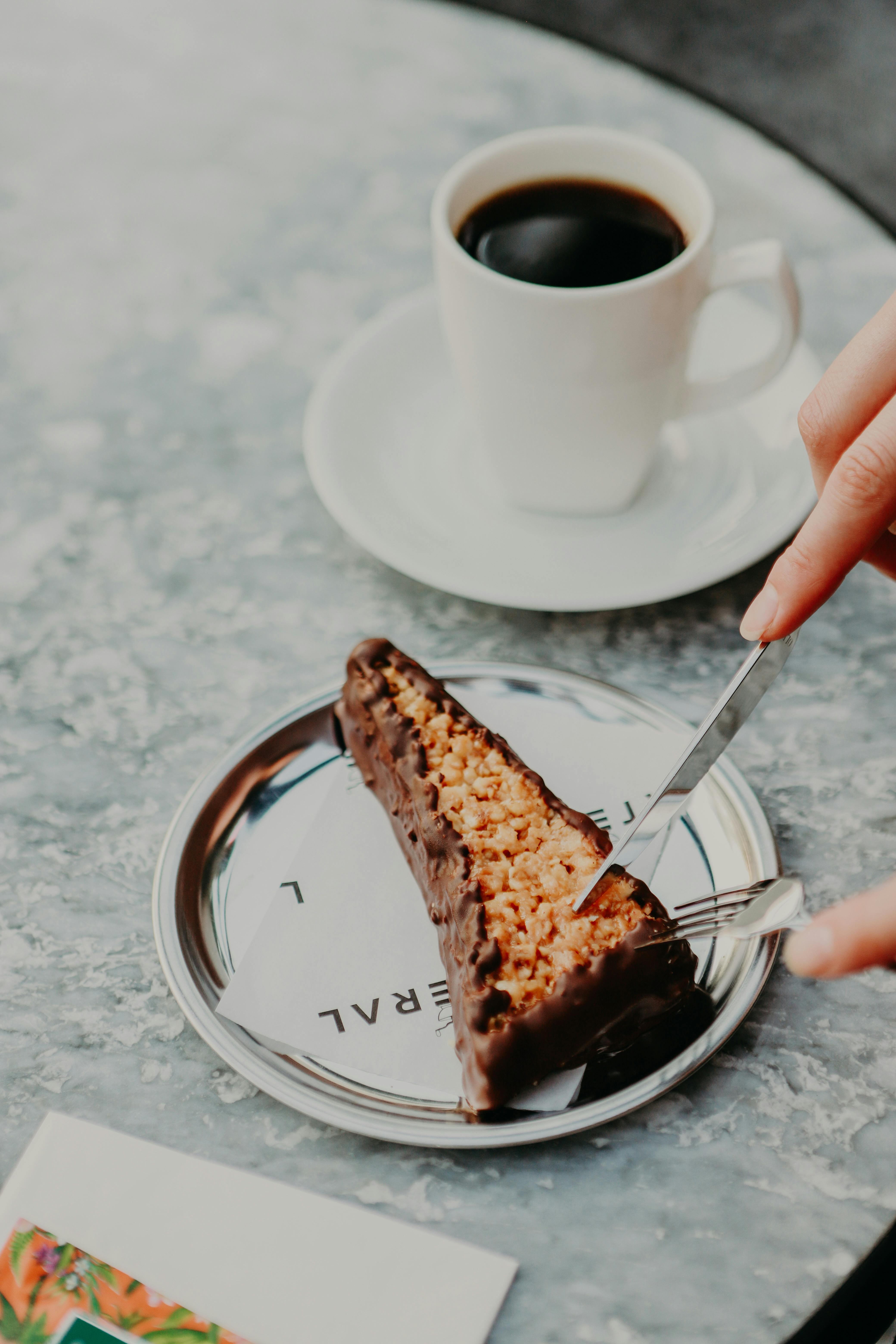A slice of chocolate-coated crunchy dessert served with coffee; a perfect indulgence.