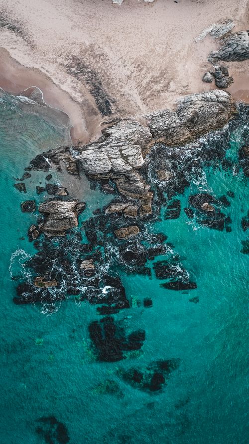 Free Stunning aerial shot of rocky beach with clear turquoise waters and dramatic waves. Stock Photo