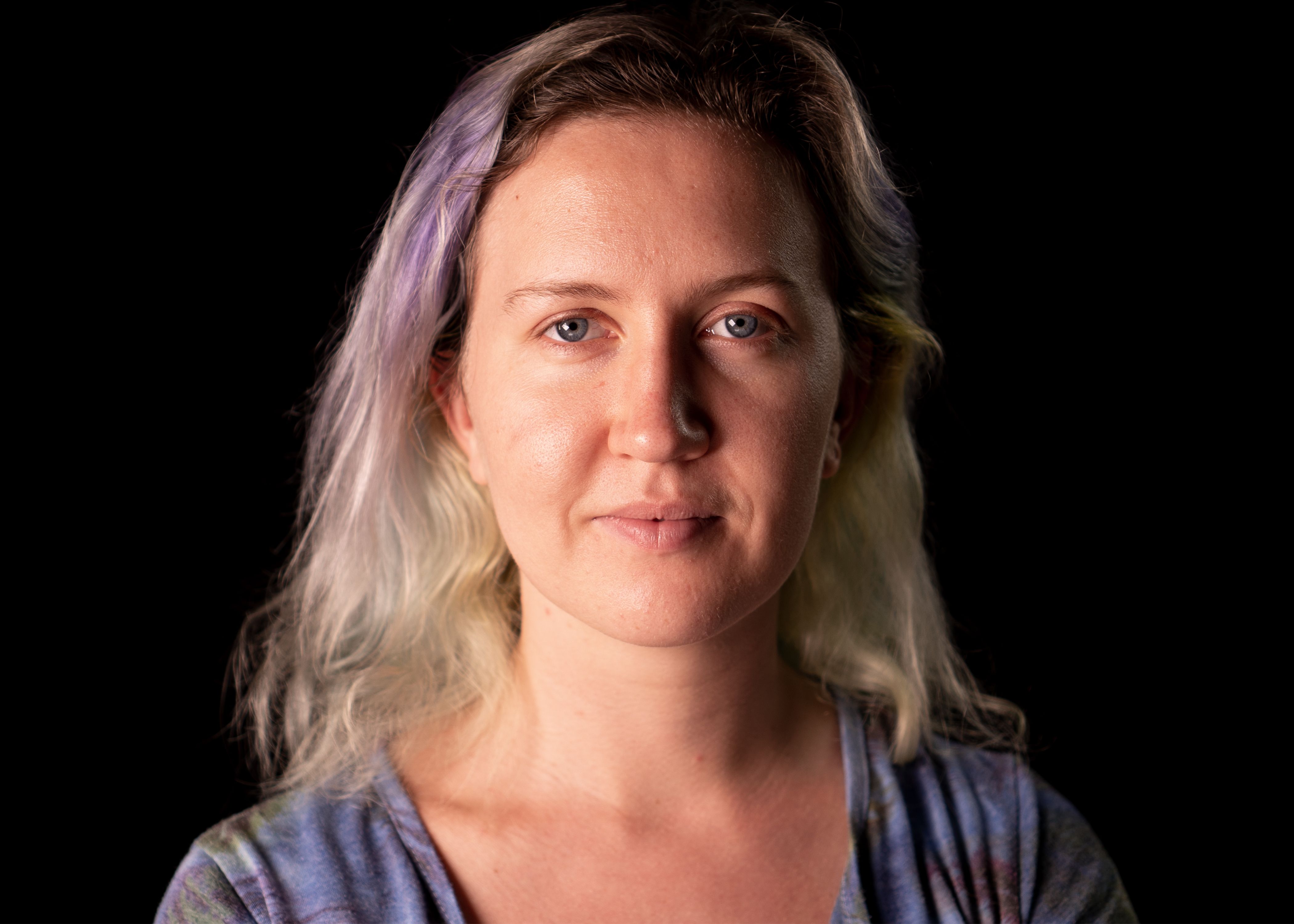 Portrait of a young woman with purple hair in a studio on a black background.
