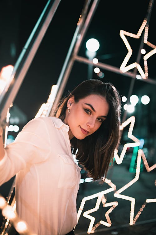 Free Woman in White Long Sleeve Shirt Standing Beside Star Shaped Lights Stock Photo