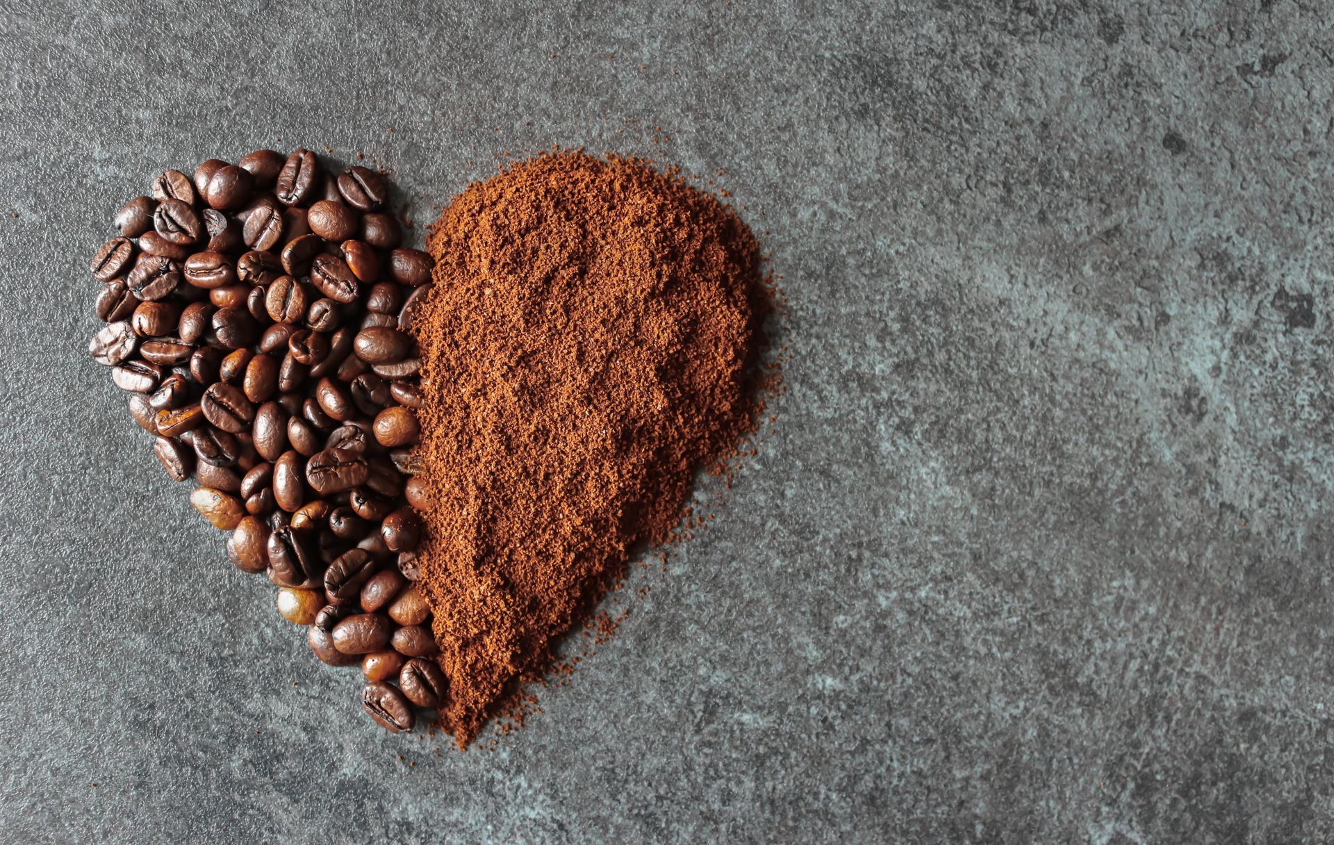 A heart-shaped arrangement of coffee beans and ground coffee on a textured surface.