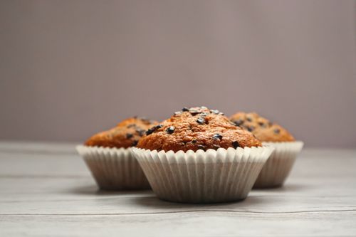 Free Tasty chocolate chip muffins placed on a wooden table, perfect for dessert lovers. Stock Photo