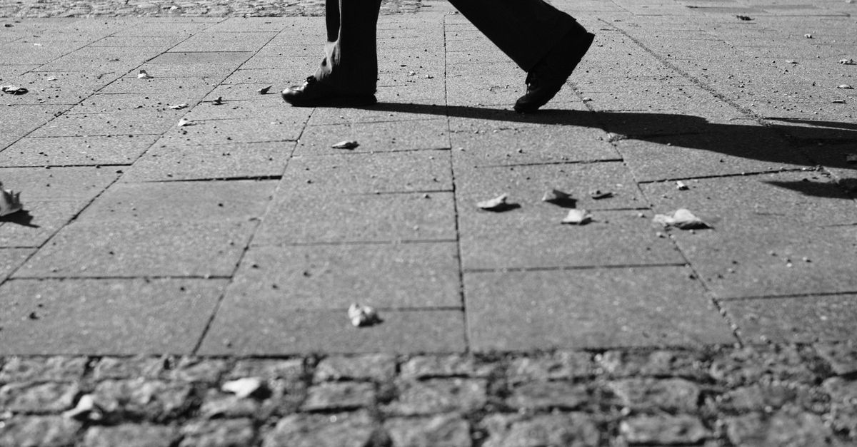 Monochrome street view capturing a person walking on cobblestone pavement in Munich.