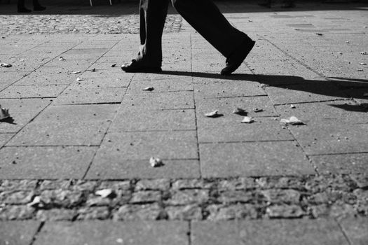 Monochrome street view capturing a person walking on cobblestone pavement in Munich.