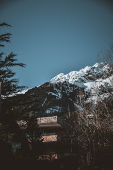 在奥地利因斯布鲁克，冬日晴空下，白雪覆盖的山峰与一座质朴的小屋构成了一幅宁静的画面