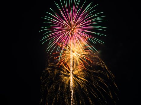 Colorful fireworks burst with vibrant trails, celebrating a nighttime festival.