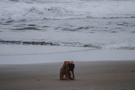 Woman in swimsuit practicing yoga on the sandy beach of Itacaré, Brazil.
