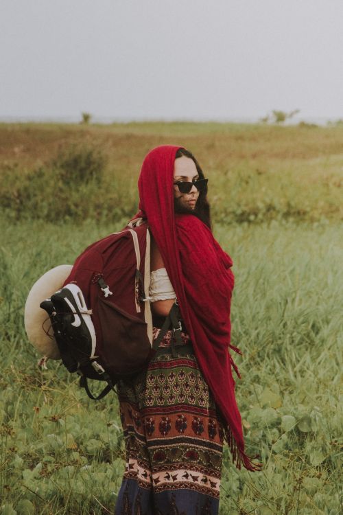 Free A woman in a red headscarf with a large backpack stands confidently in a lush, green field. Stock Photo