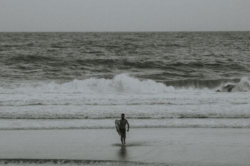 Free A lone surfer carrying a surfboard on a monochrome beach in Itacaré, Brazil. Stock Photo
