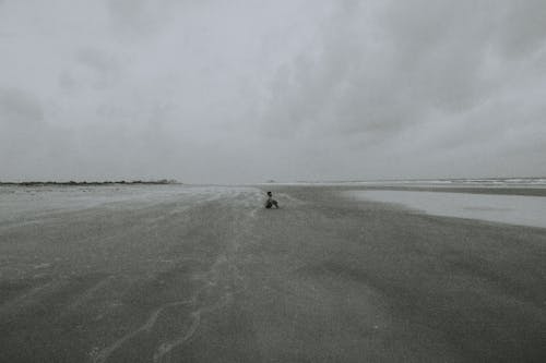 Grayscale Photo of a Person Sitting at the Beach