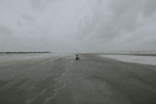 Free A lone person sits on the vast sandy beach of Ilhéus under a cloudy sky, captured in black and white. Stock Photo