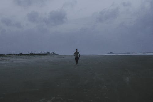 Photo of a Shirtless Man Walking at the Beach
