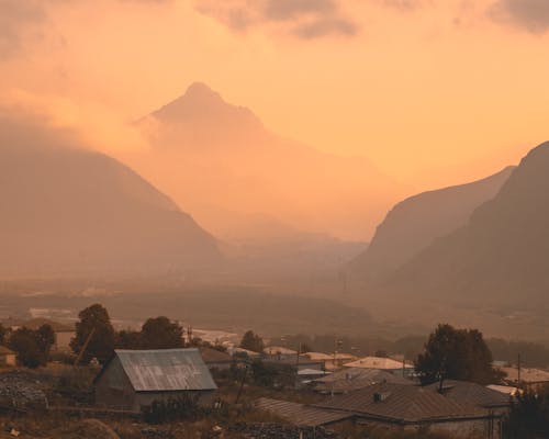 Free A breathtaking view of a mountain valley shrouded in mist and sunset colors over rooftops. Stock Photo