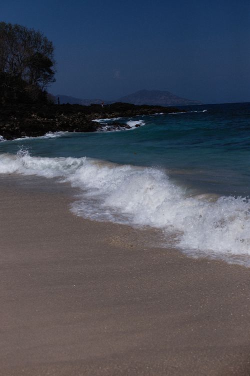 Free A serene beach scene with gentle waves crashing onto the shore and clear blue skies above. Stock Photo