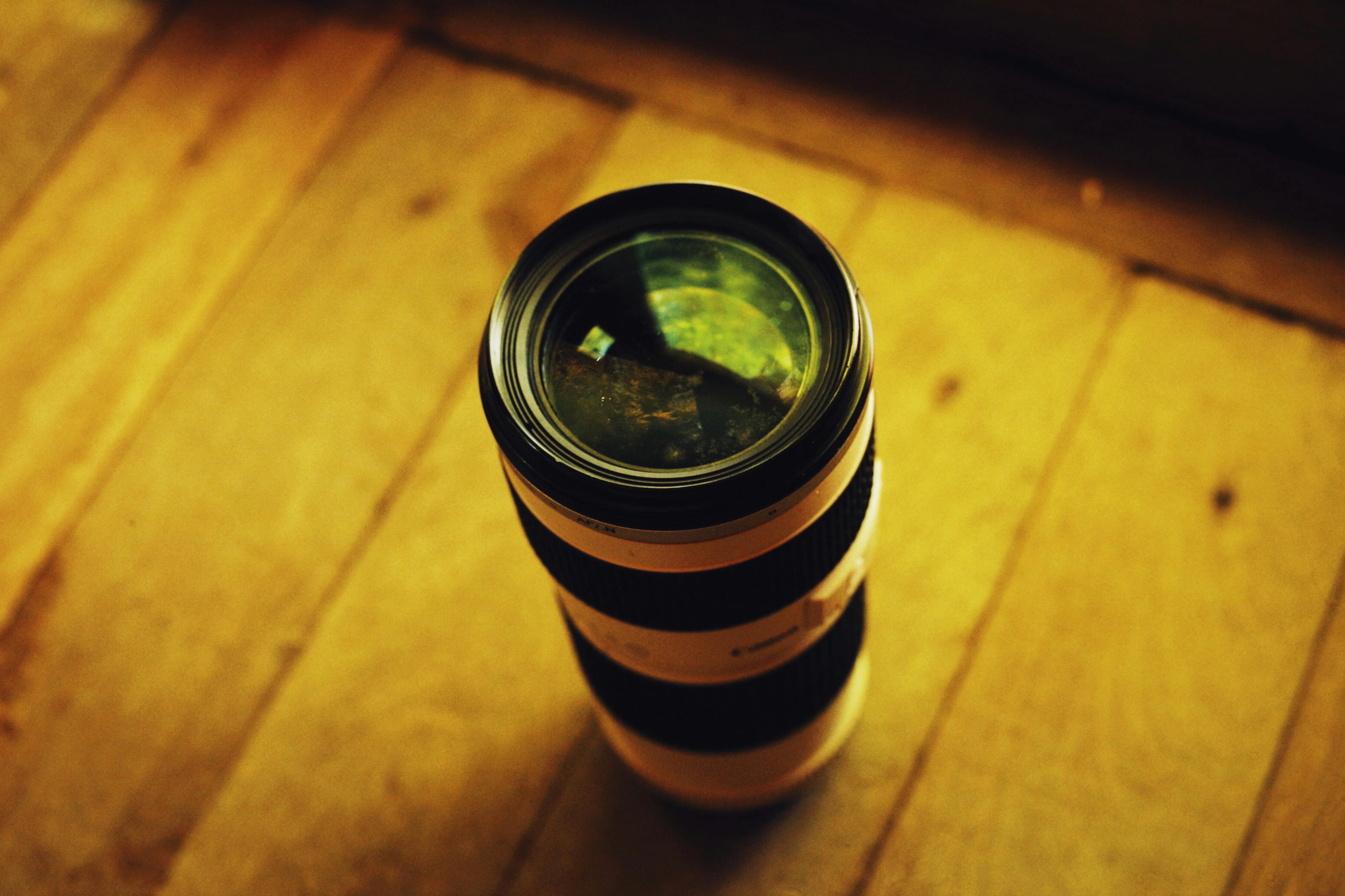 High-angle close-up of a zoom lens placed upright on a wooden floor.
