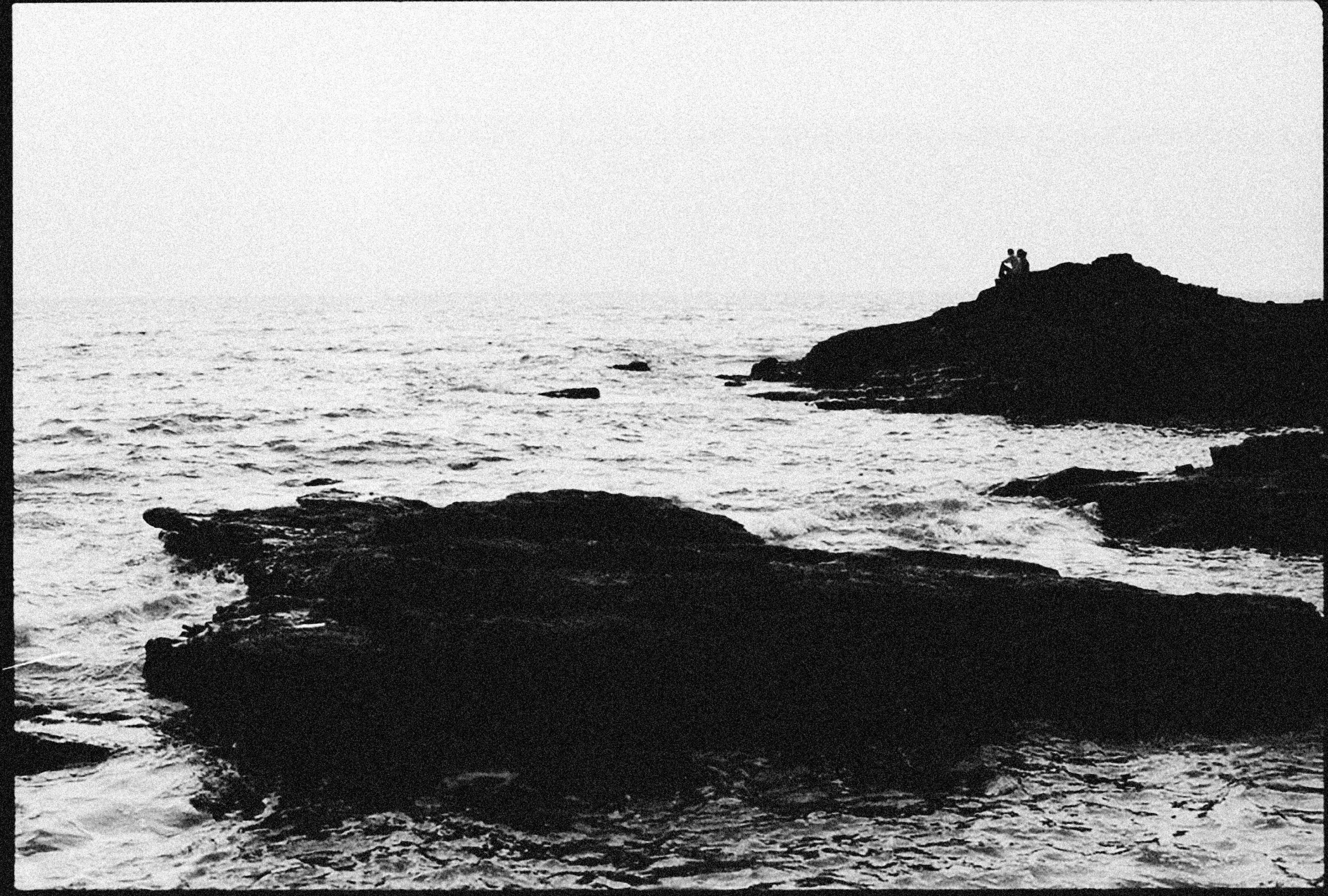 Black and white coastal scene with waves and rocky cliffs.