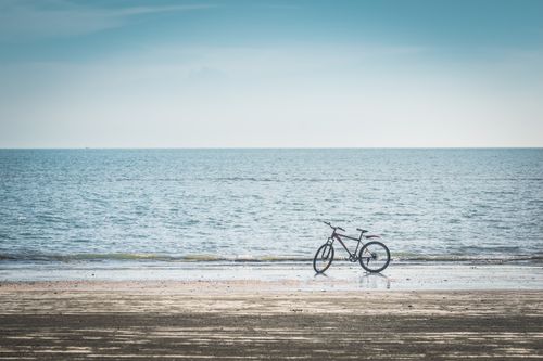 Free A solitary bicycle rests by the seashore under a clear blue sky, capturing serenity and solitude. Stock Photo